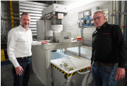 Simon Wagenaar, manager of the technical services department for coating at Ulamo Coating BV and Robin Rohde, account manager at Rösler Benelux, is standing in front of the full-automatic centrifuge that cleans the pre-treatment liquids from two tanks